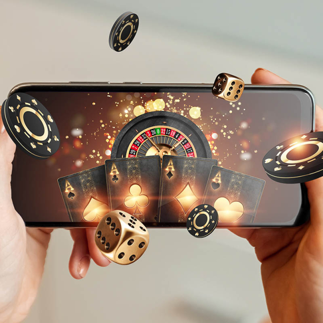 Creative background, online casino, in a man's hand a smartphone with playing cards, roulette and chips, black-gold background. Internet gambling concept. Copy space.